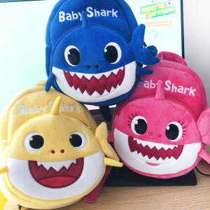 3 plyschryggsäckar för barn som föreställer en söt haj. Den här är placerad på ett platt bord