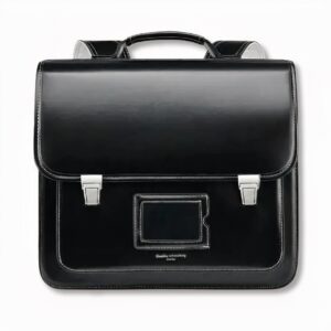 Cartable noir d'écolier traditionnel avec un porte carte devant, sur fond gris clair